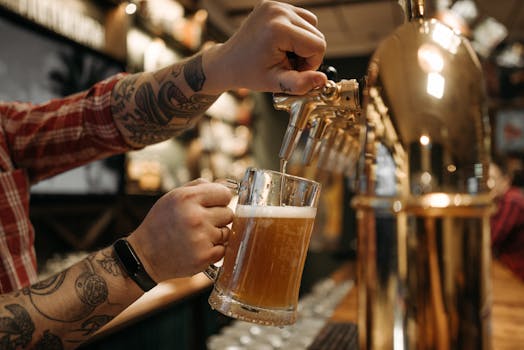 Close-up of a bartender pouring a cold draft beer into a glass mug at a bar.